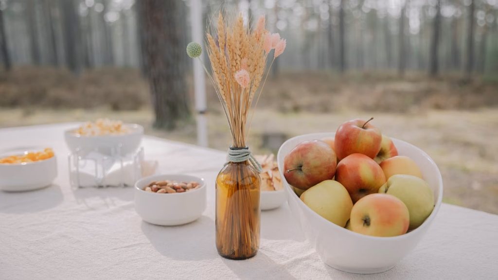 Rustic outdoor table setup featuring apples, nuts, and dried flowers in a vase, creating a cozy autumn vibe.